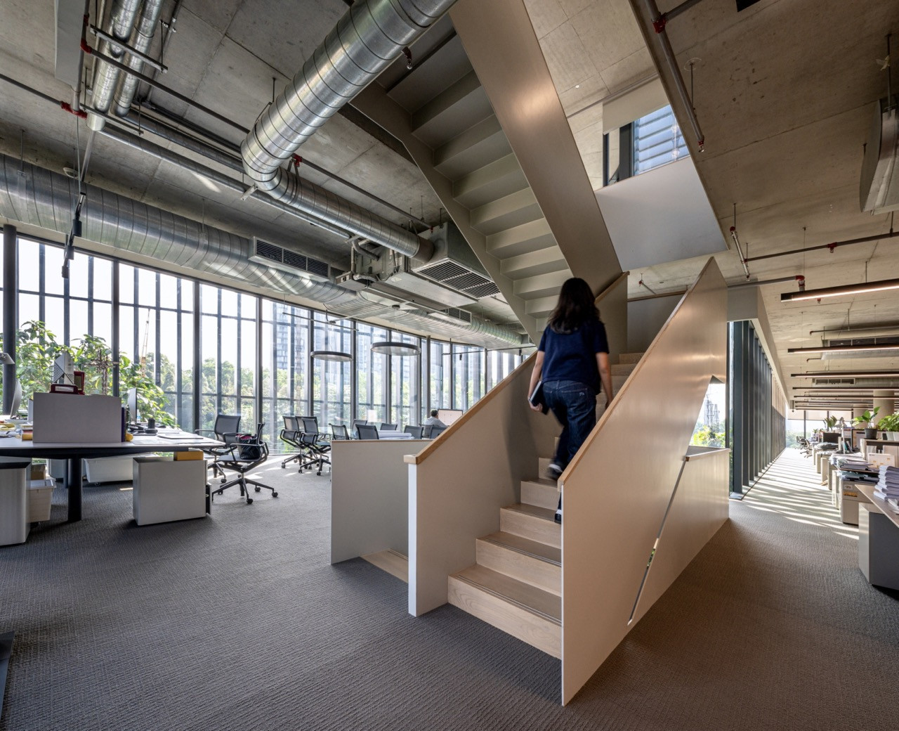 The multi-level workspace at GDP Campus features exposed concrete ceilings, open stairs, and abundant natural light, designed to foster collaboration and chance encounters between different design teams and studios