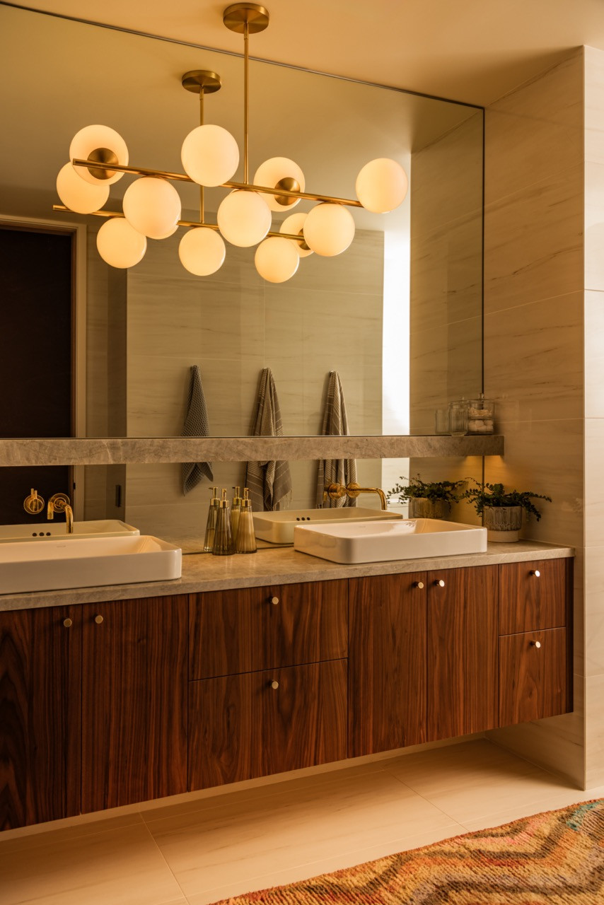 A Luke Lamp chandelier illuminates the primary bathroom’s double vanity with walnut cabinetry and brass hardware