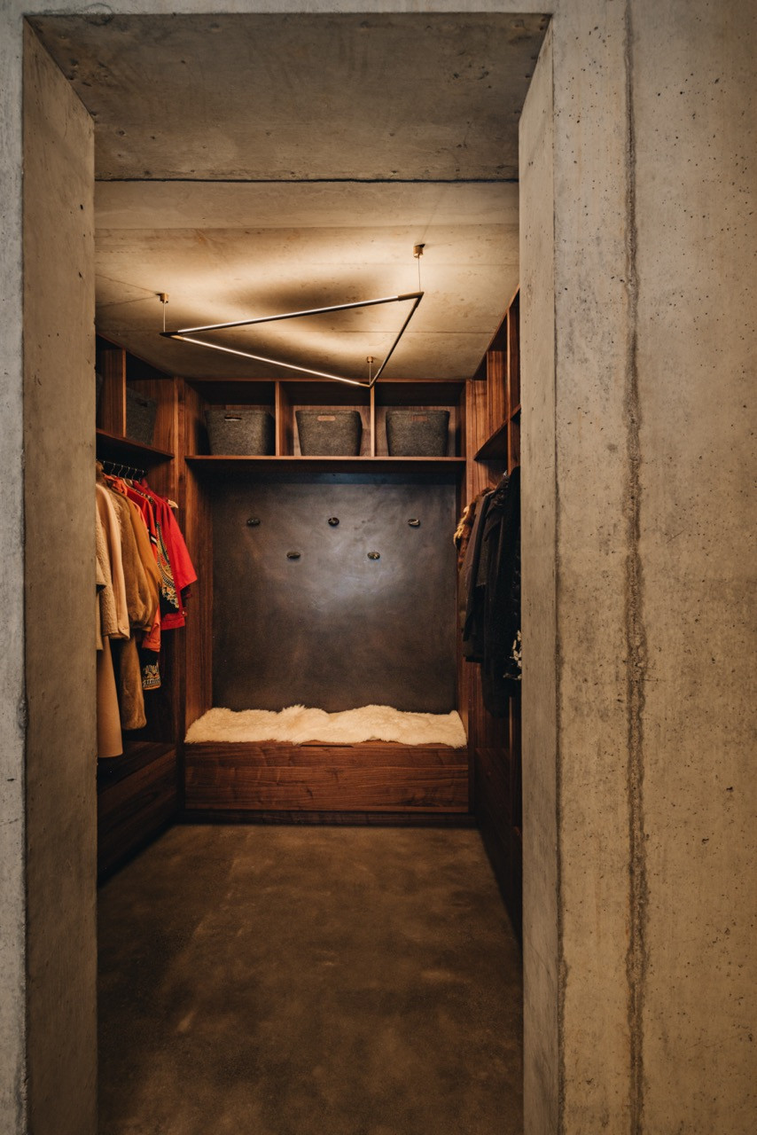The primary closet entrance features raw concrete framing and walnut millwork, with concrete floors that incorporate metal veining