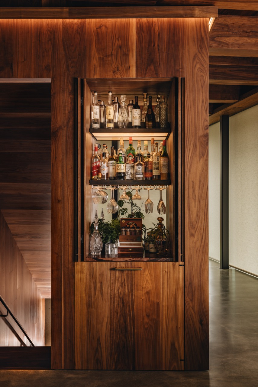 The wine bar includes custom lighted shelving by Jordan Hufnagel, built into walnut millwork, storing the couple’s collection from their Corollary Wines business