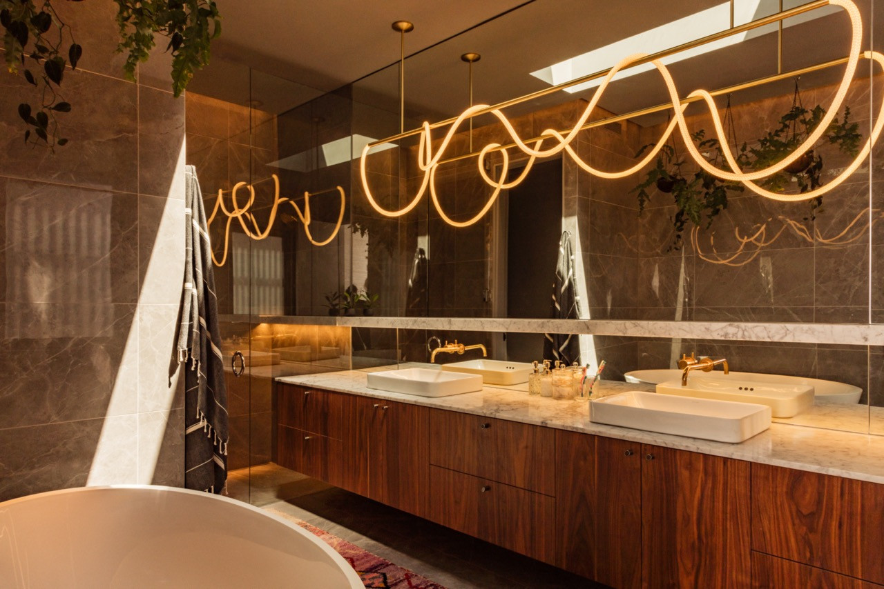 The primary bathroom includes a sculptural pendant light, walnut vanity cabinetry, and dark stone surfaces with Vola fittings
