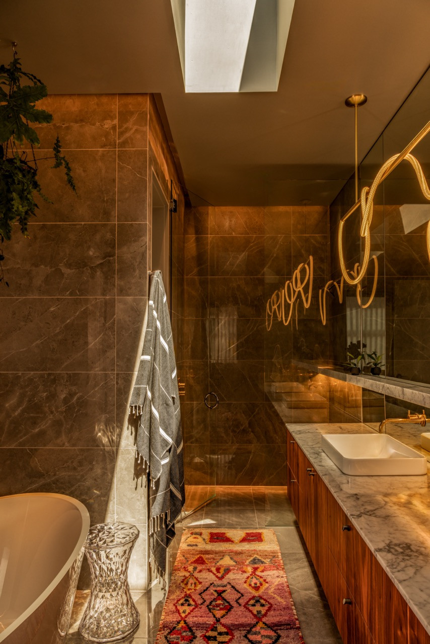 The primary bathroom includes sculptural pendant lighting, dark stone surfaces, walnut cabinetry with unlacquered brass hardware, and a vintage runner from Benisouk