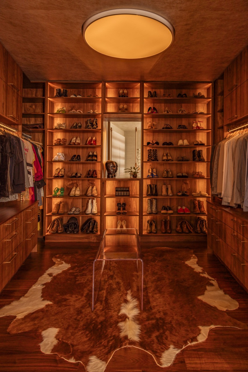 The primary closet features a Prudential oculus light, custom walnut millwork, and a Kush rug with cowhide pattern on the concrete floors with kintsugi-inspired metal veining
