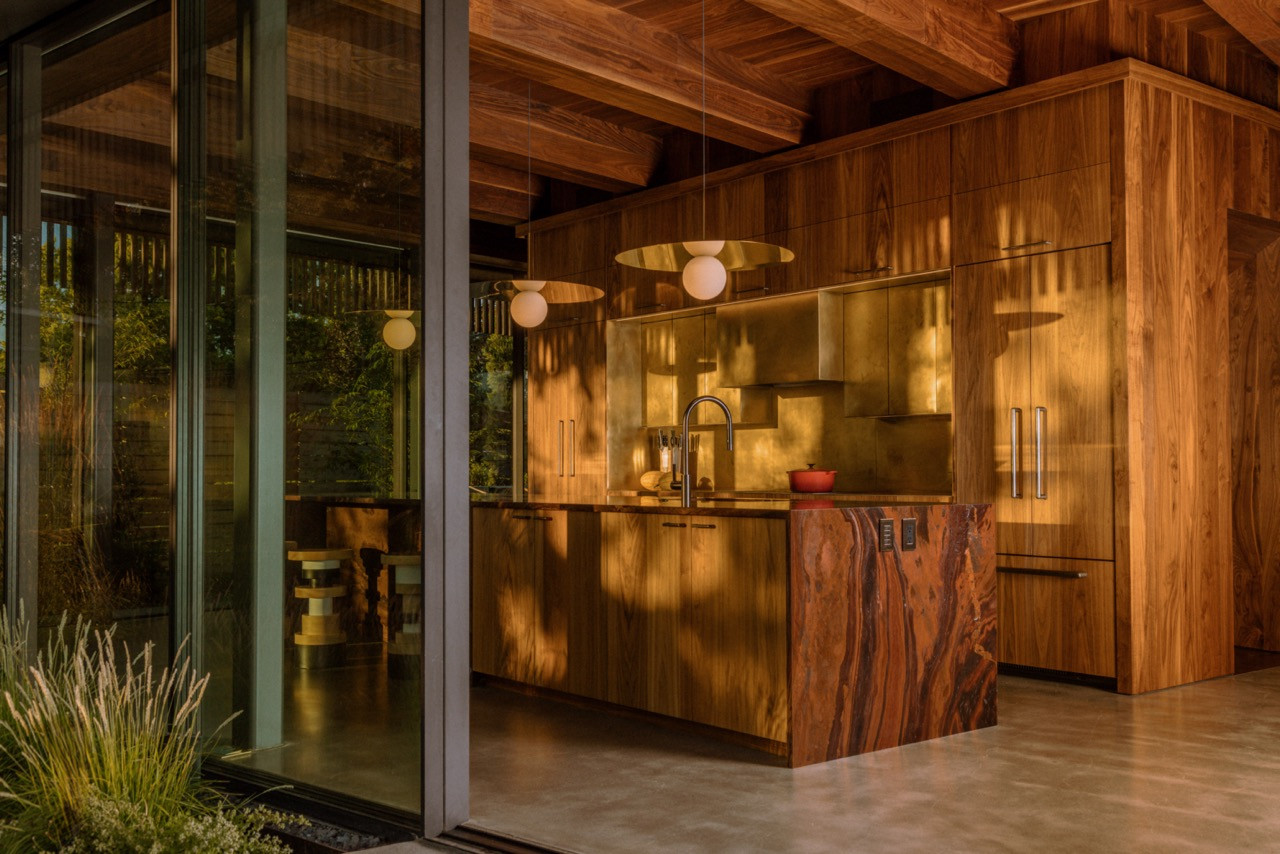 The kitchen includes walnut cabinetry by Earthbound Industries, Pablo pendants, and floor-to-ceiling glass walls opening to the garden