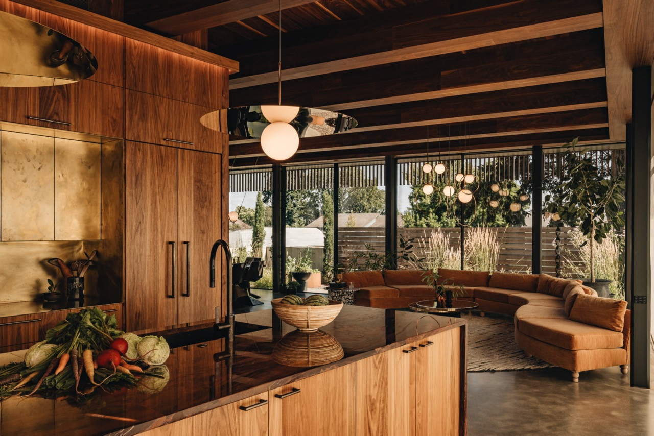 The main level features a vintage Milo Baughman sofa reupholstered in Lee Jofa fabric, a Pablo chandelier, and walnut millwork by Earthbound Industries, all set against floor-to-ceiling glass walls