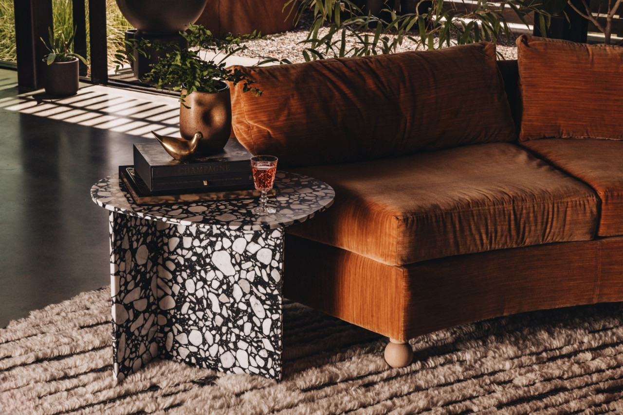 The living area includes a vintage coffee table with natural stone patterns, a reupholstered Milo Baughman sofa in Lee Jofa fabric, and a Kush rug