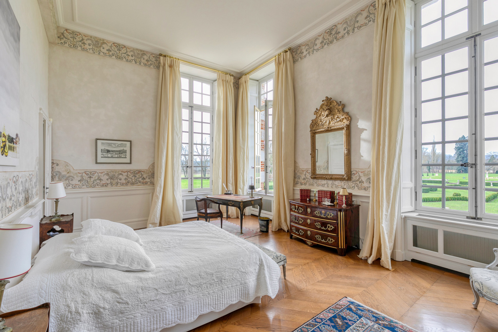 Master bedroom featuring tall windows and period details, part of the château's 17 bedrooms within the carefully restored historic residence