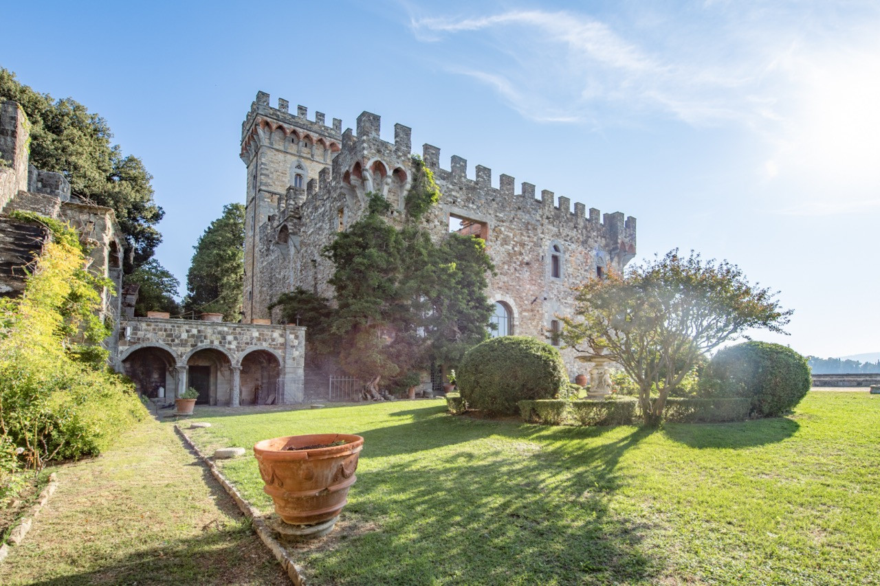 The main castle at Castello di Vincigliata rises above the estate gardens and featuring the distinctive tower and castellated walls of this historic European castle restored by John Temple Leader in the 1850s-1860s