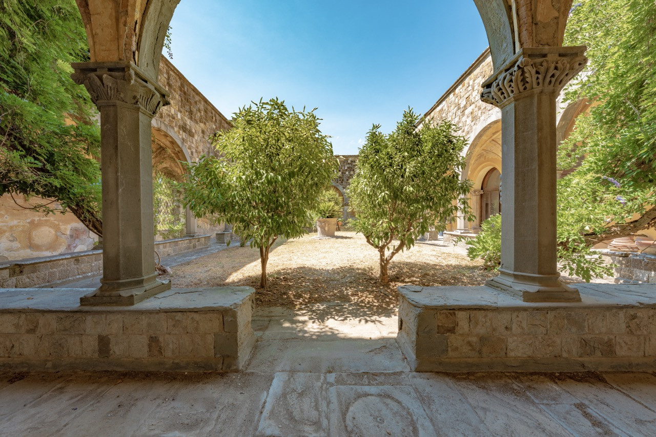 The historic cloister at Castello di Vincigliata features carved stone columns and arched walkways, reflecting the castle’s connection to its origins on the site of a former medieval settlement