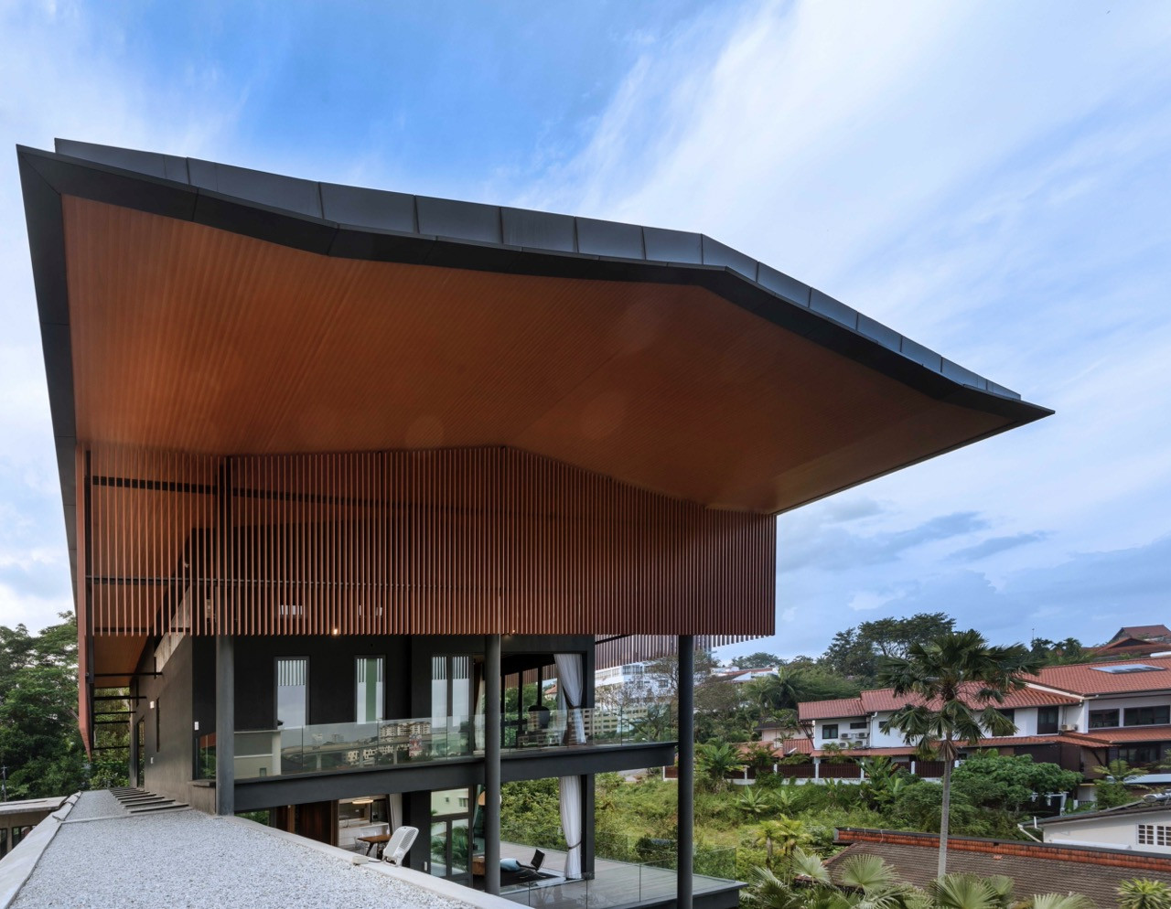 Dramatic view of curved roof overhang with timber screens protecting glazed facades from tropical sun