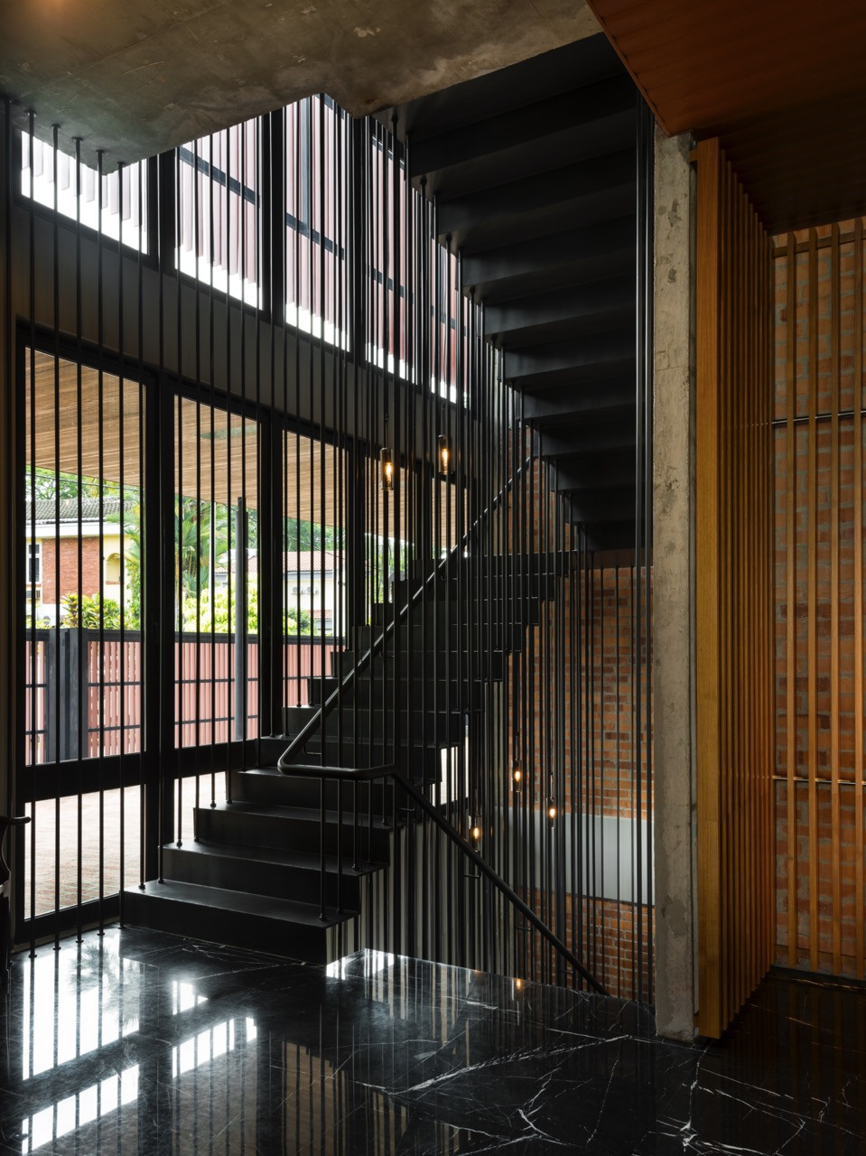 Steel staircase through the central core, enclosed by vertical metal screens creating shadow patterns on the clay brick walls