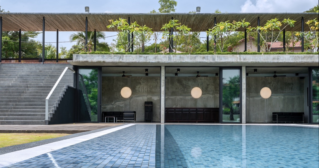 Swimming pool with off-form concrete walls, planted roof terrace above, and continuous glazing to interior spaces.