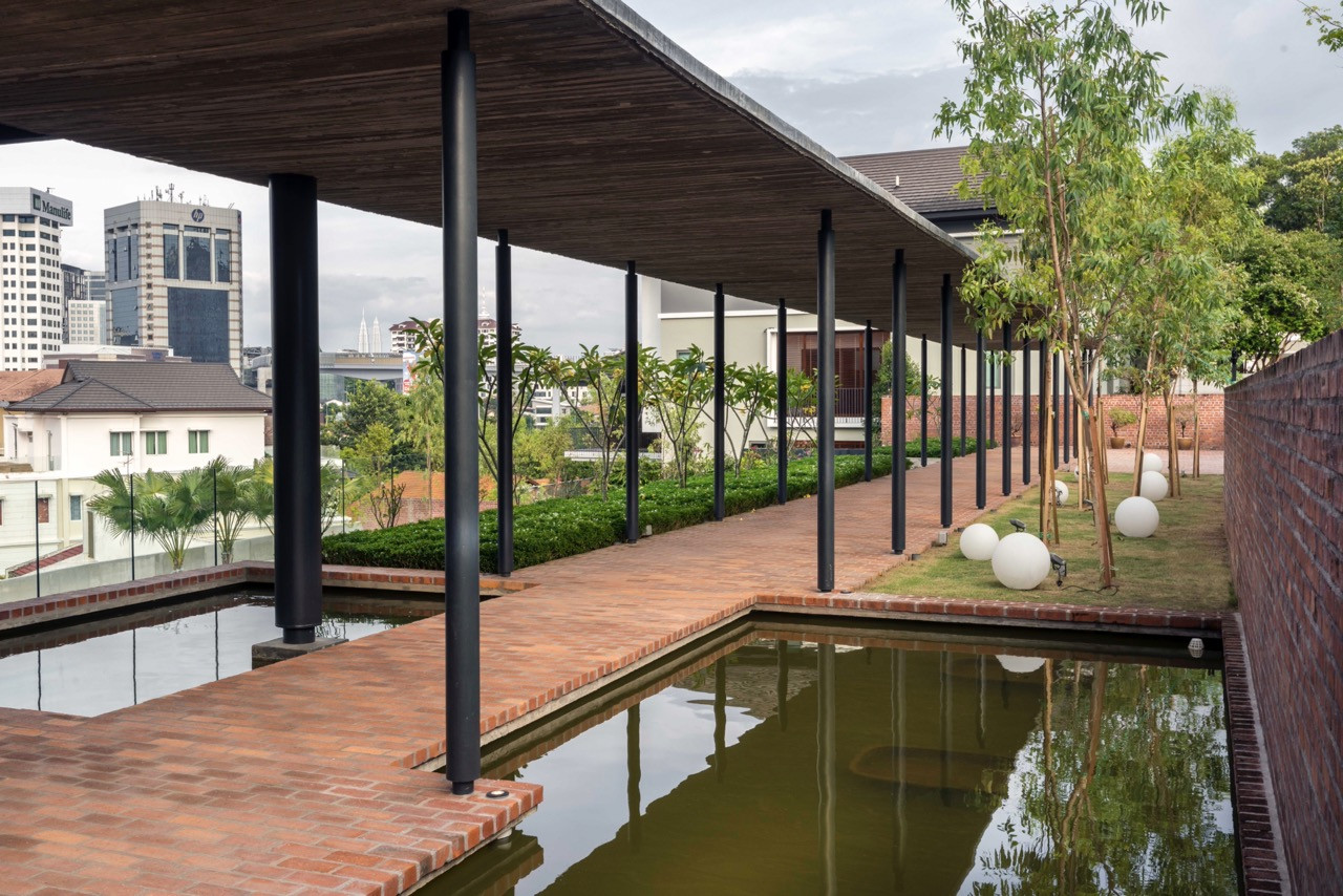 Verandah extending toward Kuala Lumpur with reflecting pools and planted gardens softening architectural geometry