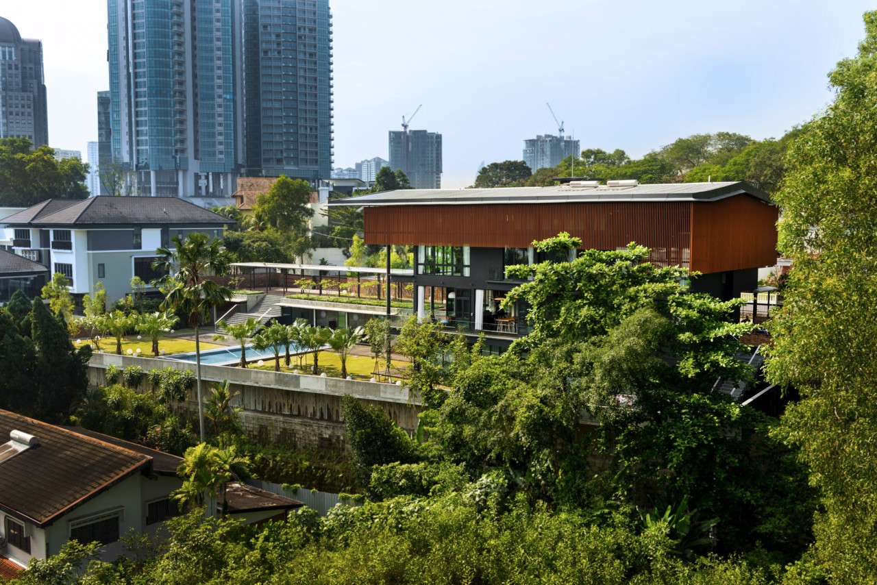 Aerial view revealing hillside siting with pool at the lowest level and living spaces under an overhanging timber roof