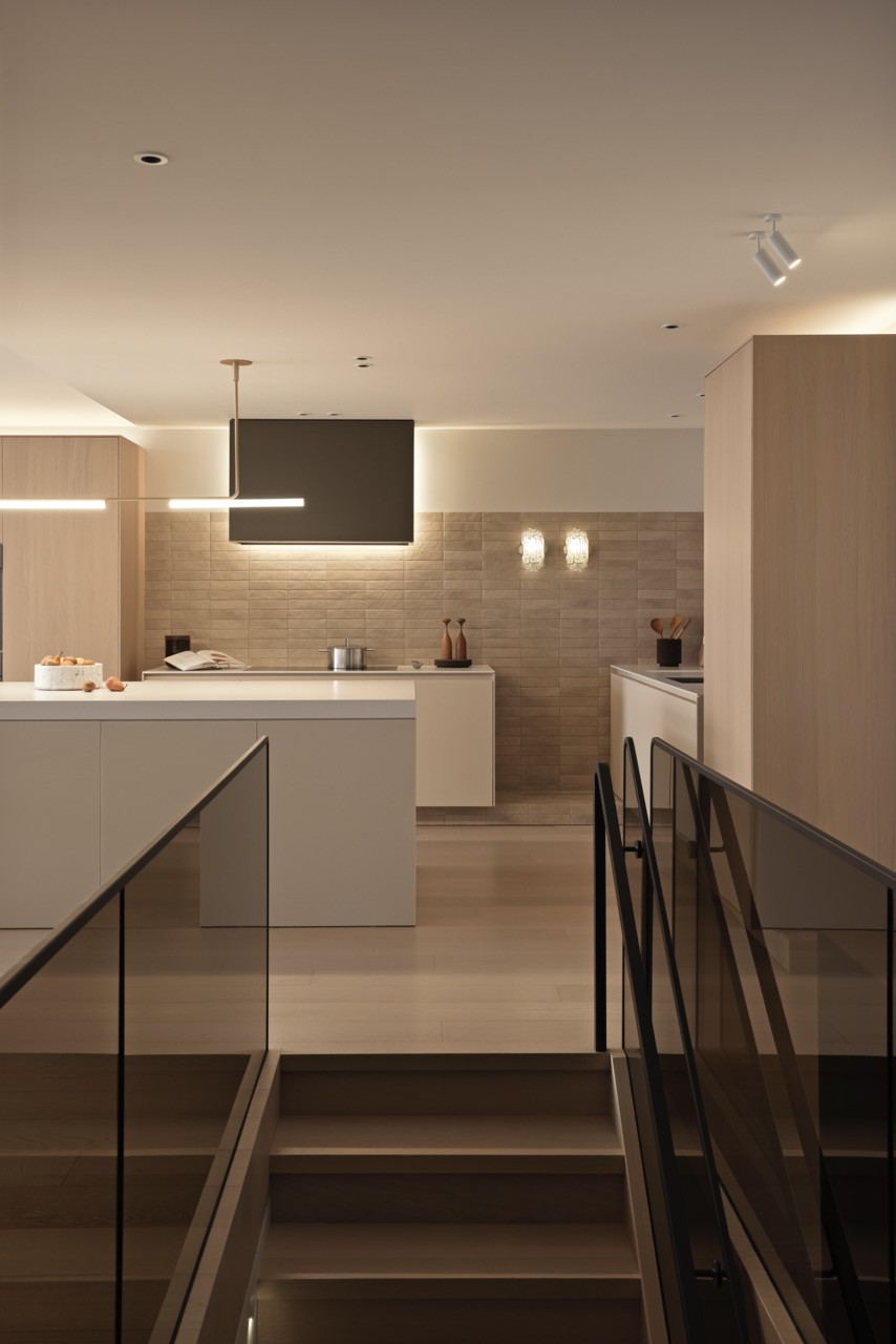 The bronzed glass stair guard defines separate zones whilst maintaining visual connection throughout the open-plan spaces, with Spanish porcelain tile forming the kitchen backsplash