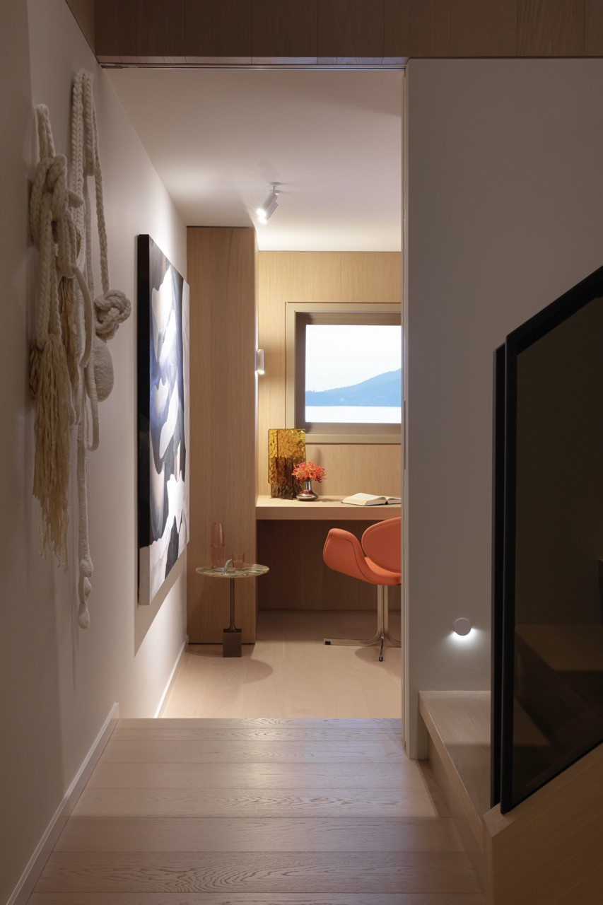 The entry hallway showcases a textile sculpture by Fei Disbrow on the stairway wall, with views through to the office nook featuring an orange chair and built-in desk overlooking Burrard Inlet