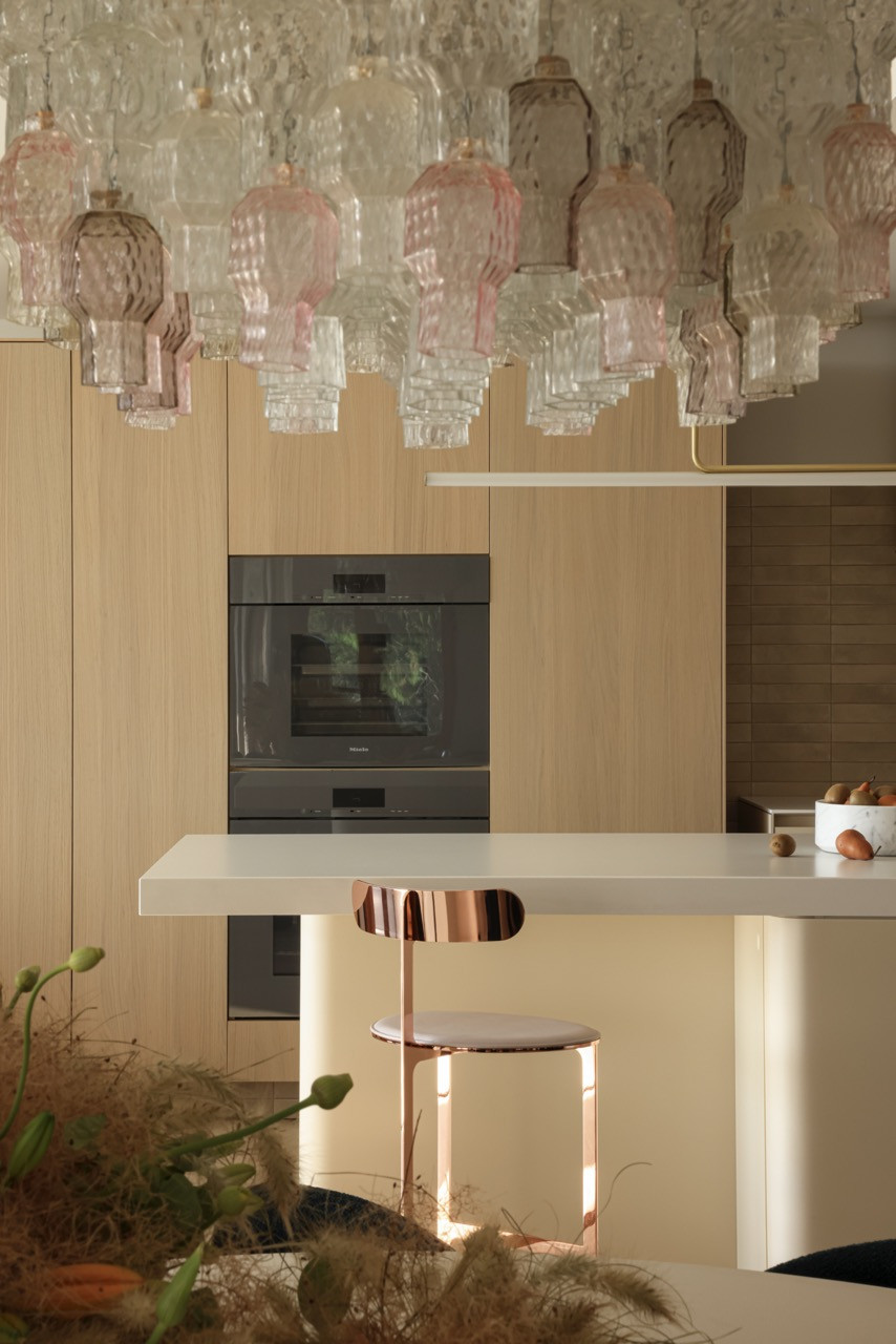 The kitchen features vintage Murano glass chandeliers and light hardwood millwork, with Miele appliances integrated discretely to maintain clean lines in the open-plan design