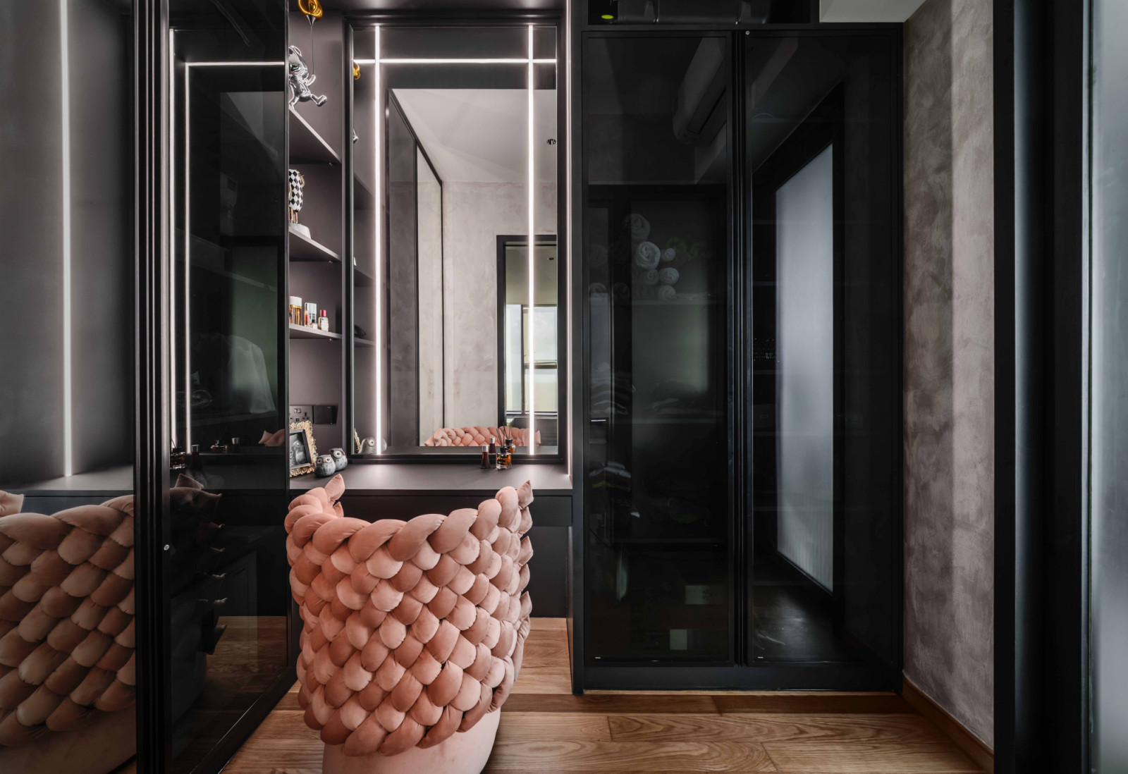 An oversized woven-texture chair in pink brings a soft touch to the otherwise sleek black vanity area