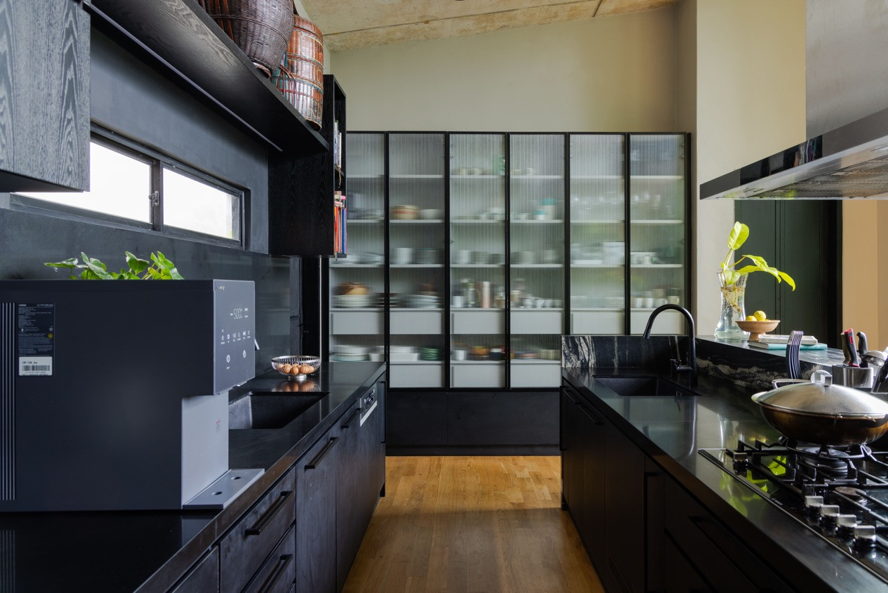 The modern kitchen features dark cabinetry and stone countertops, with fluted glass storage systems