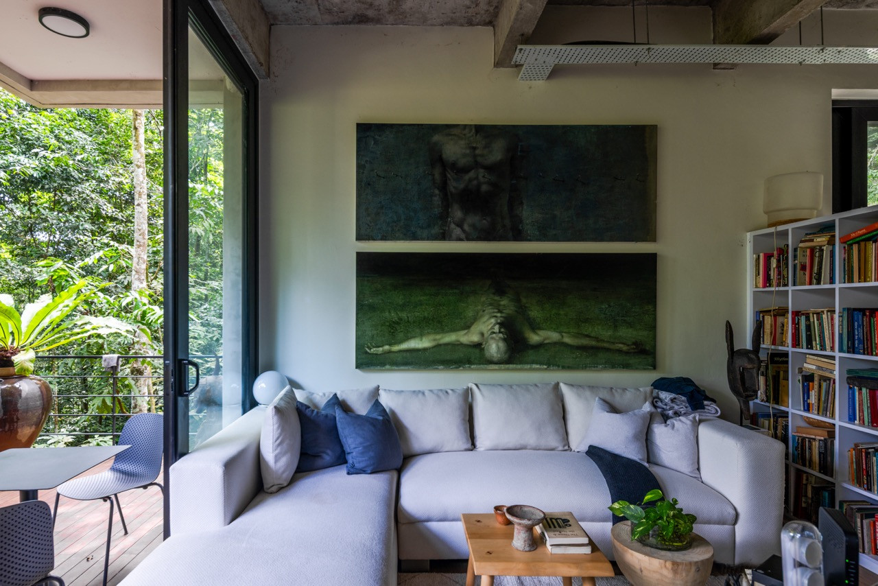 The living area demonstrates the interplay between cool concrete and warm timber grains, with floor-to-ceiling windows opening to the forest and providing gallery wall space for the artist owners' curated collection.