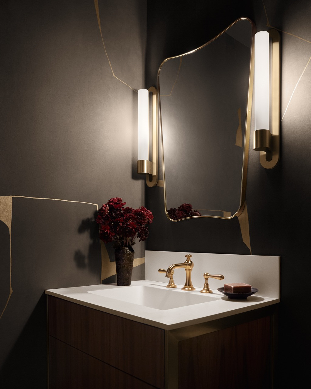 A powder room features brass sconces by Urban Electric, flanking an organic-shaped mirror, which demonstrates the design team’s commitment to unusual lighting choices