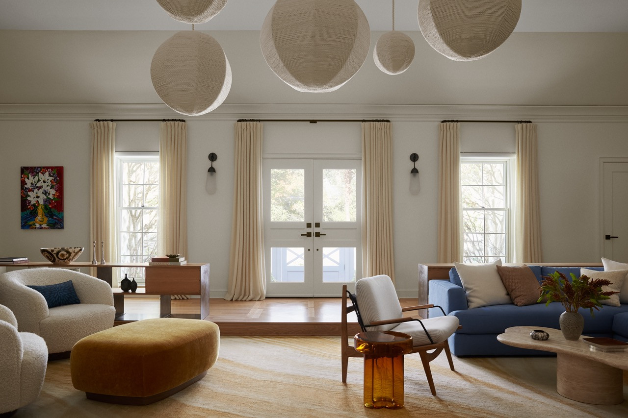 The stepped-down living room serves as the home's neutral hub, painted in warm white whilst saturated colours radiate outward which is an unusual approach for Main Line interiors