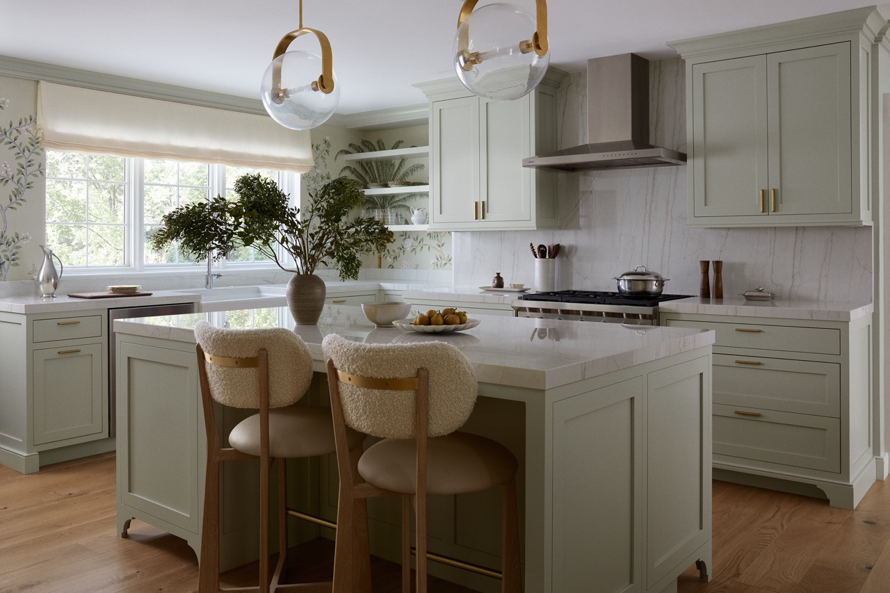 The kitchen in Farrow & Ball’s minty sage “Eddy” features De Gournay’s Amazonia wallpaper and oversized pendant lights, creating an untraditional approach to suburban kitchen design
