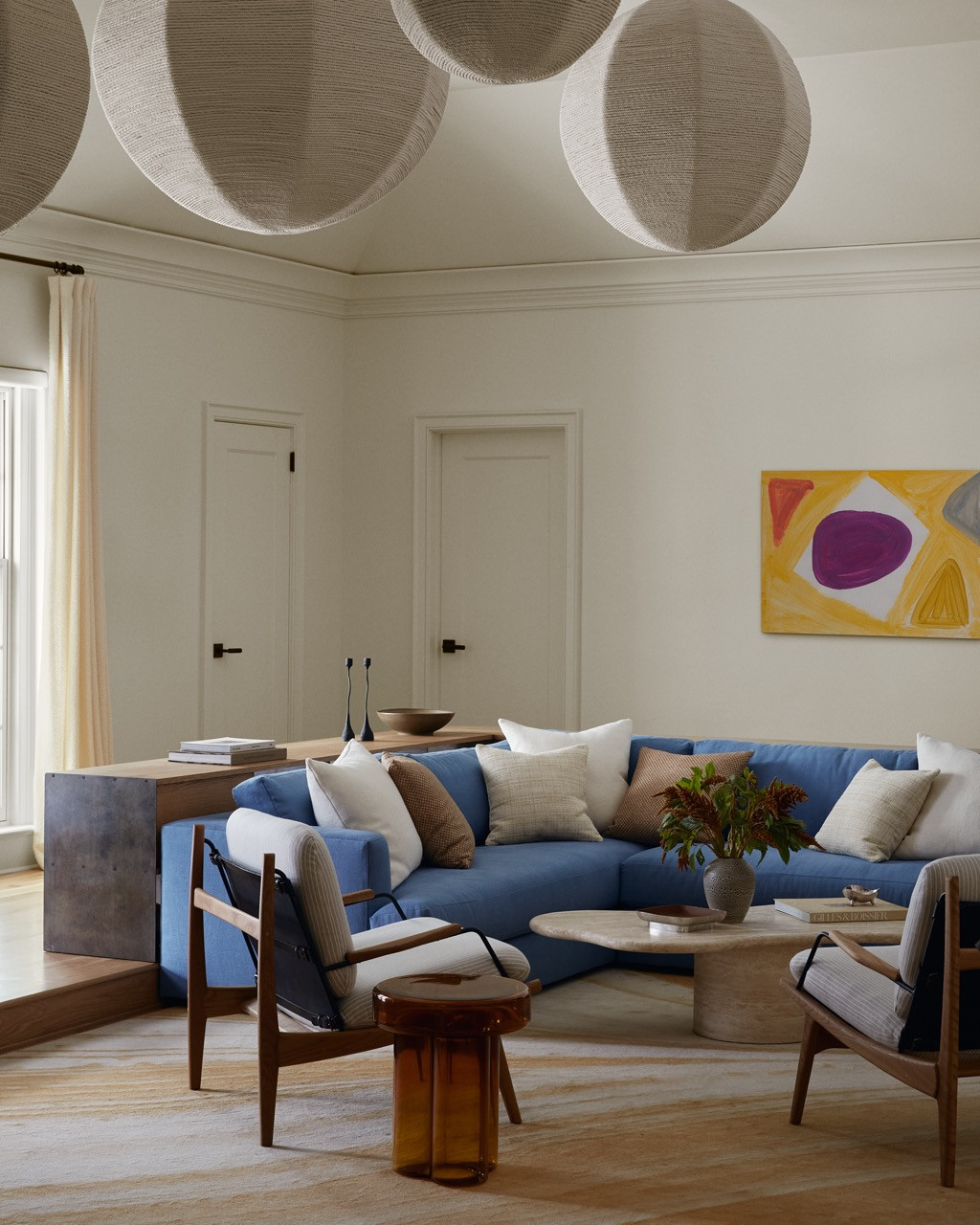 The central white living room serves as neutral territory between the home's more saturated spaces. Large globe pendants by Cuff Studio hang above vintage Czech chairs and a blue L-shaped sofa