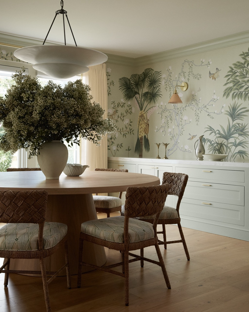 The breakfast room adjacent to the kitchen features botanical De Gournay wallpaper and woven dining chairs, blending natural materials with luxurious finishes