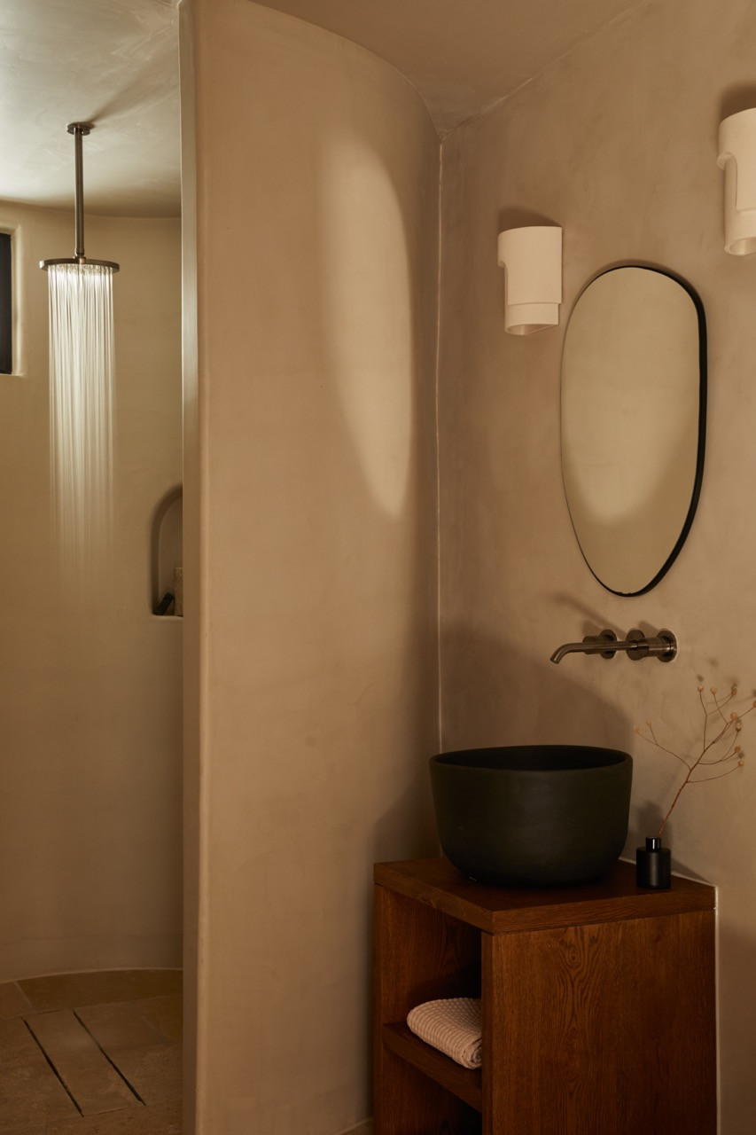 A bathroom features an arched doorway leading to a walk-in shower, with a wooden vanity supporting a matte black vessel sink