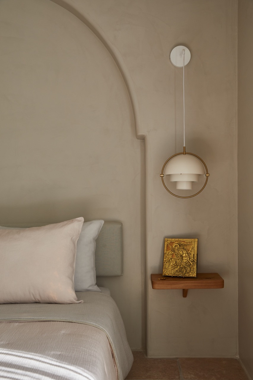 The bedroom features a brass pendant light suspended above a floating wooden shelf displaying a traditional Greek icon in gilded finish