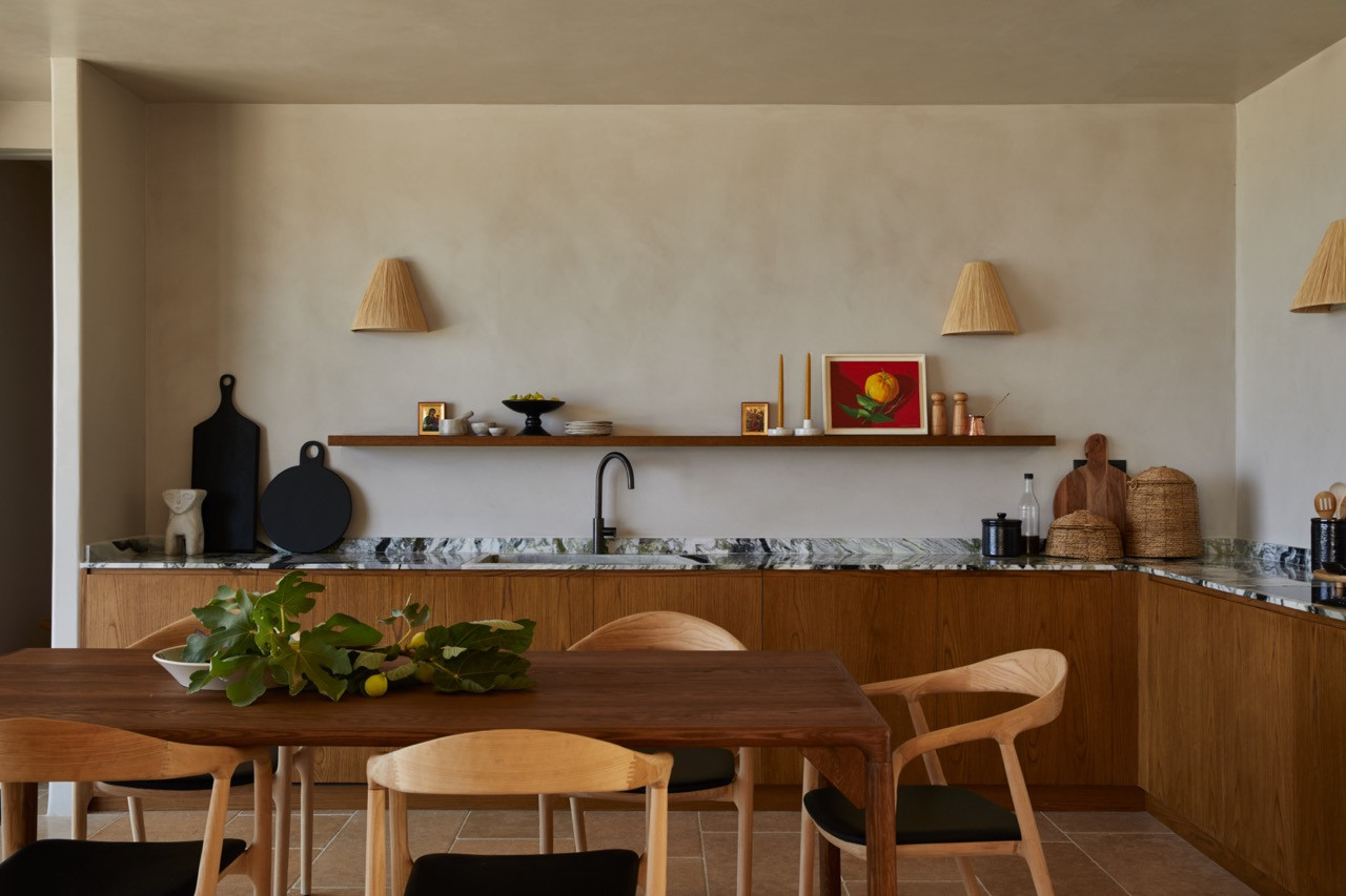 The kitchen showcases custom wooden cabinetry with marble countertops, open wooden shelving, and raffia wall sconces flanking displayed ceramics