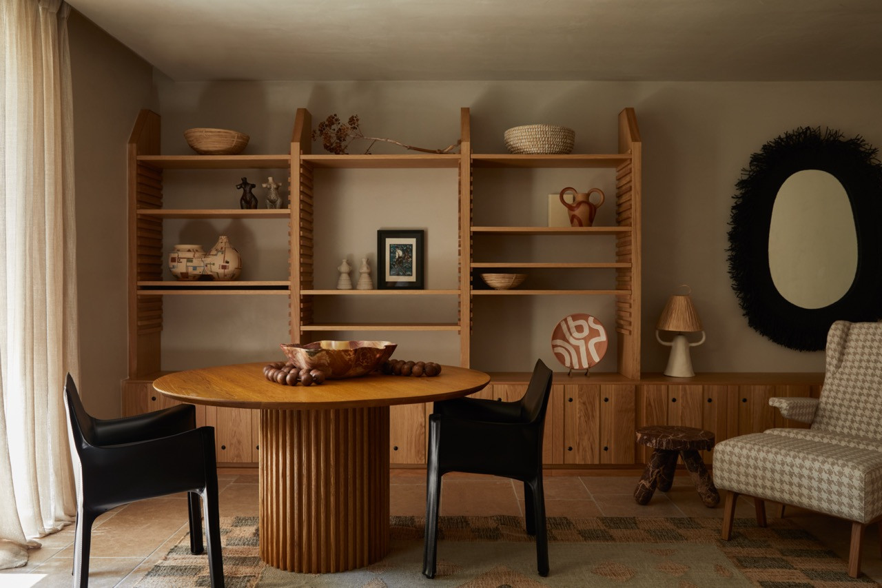 A custom round dining table with fluted base anchors the reading room, flanked by built-in wooden shelving displaying ceramics and traditional objects