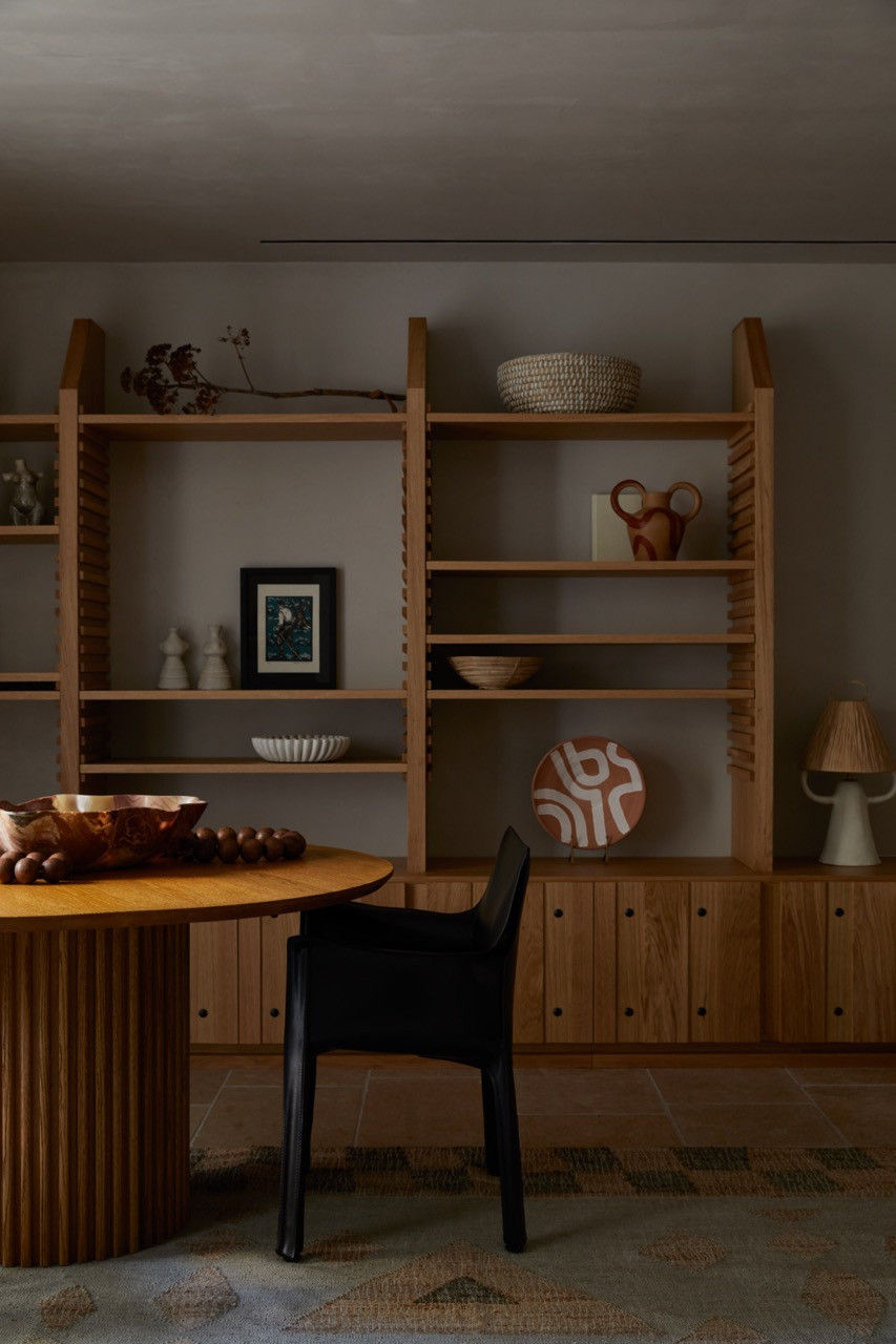 Custom wood shelving with exposed joinery displays handmade ceramics and family mementos against walls treated with traditional patiti plaster
