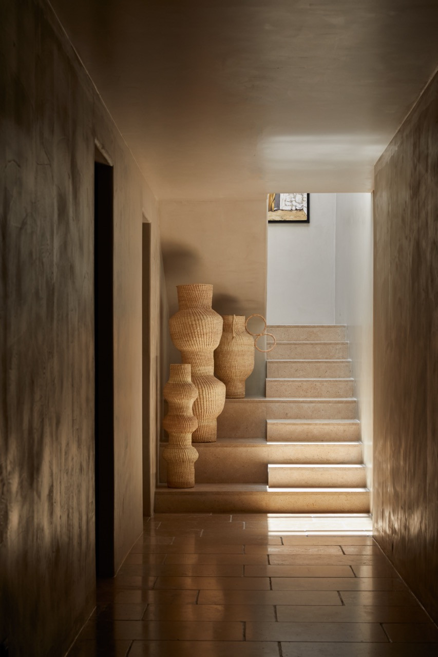 Patiti-plastered walls frame a view down the corridor where decorative woven vessels punctuate the stairs connecting different levels