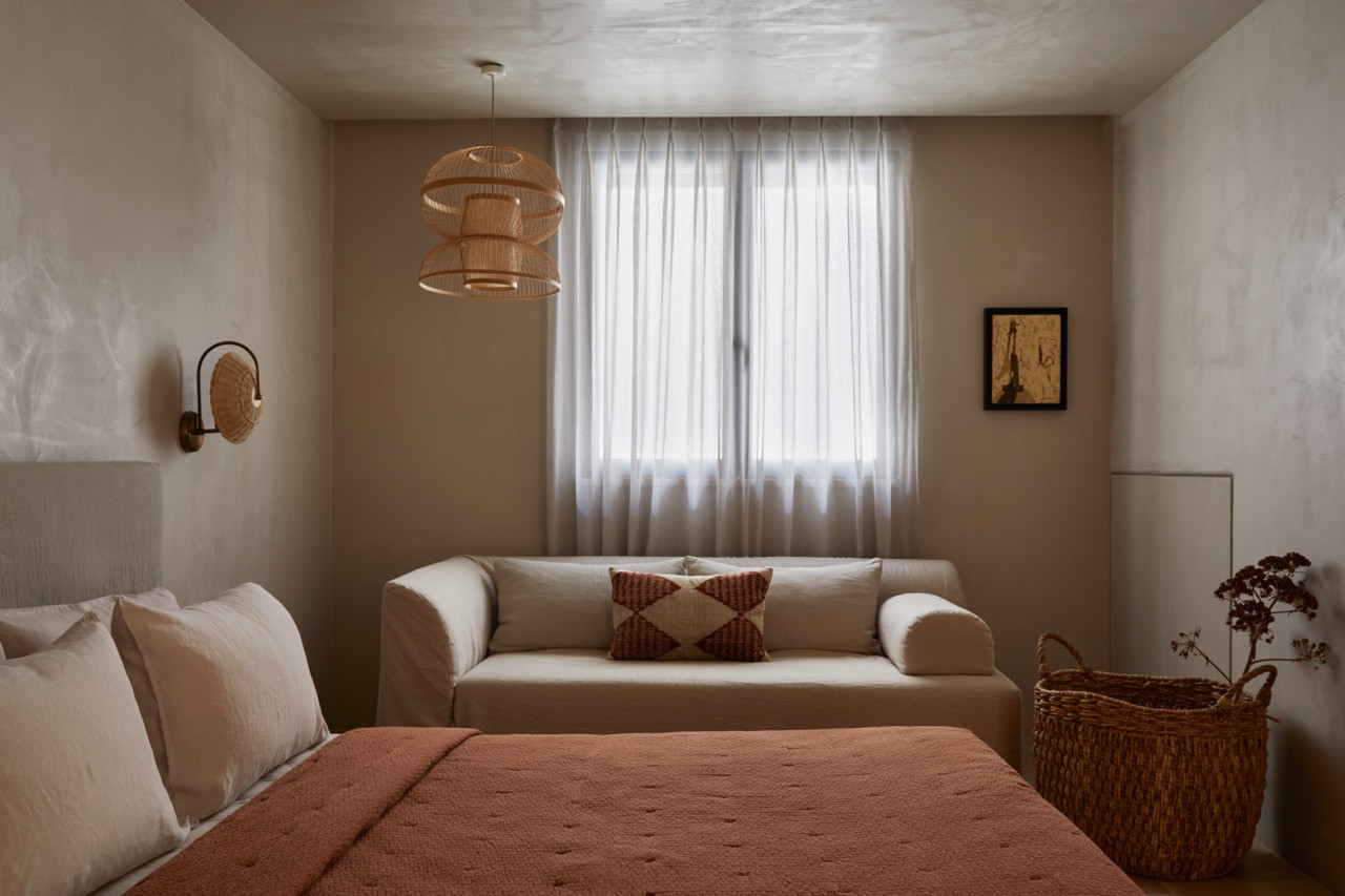 Natural linen textiles and woven rattan pendant lights create warmth in a guest bedroom designed around neutral tones and organic materials