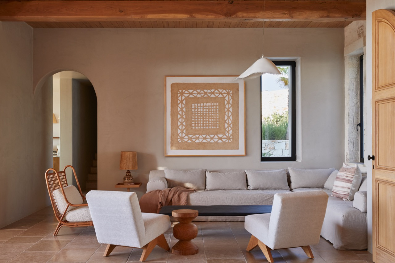 A framed textile artwork hangs above the custom sofa in the main living room, complementing the neutral palette and hand-cut wooden ceiling beams