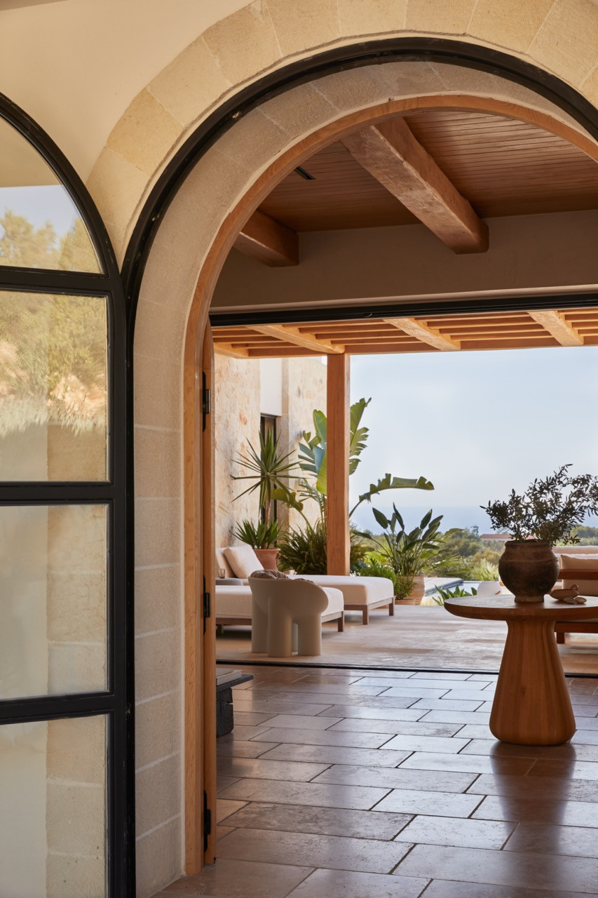 Arched passages with exposed wooden ceiling beams connect the bedroom corridors where sunlight creates dramatic patterns on the terracotta tile floors