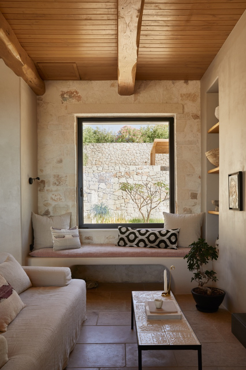 A built-in window seat beneath exposed wooden beams offers views to the stone-walled garden, upholstered in blush fabric with patterned cushions