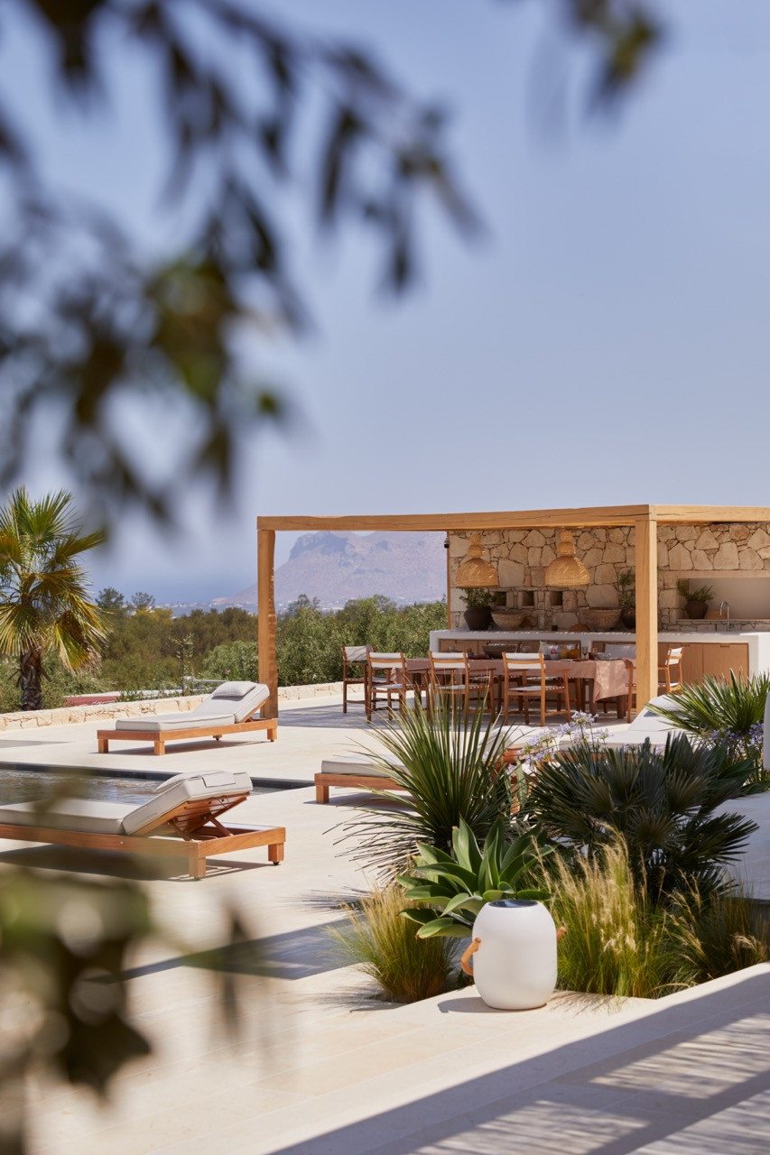 Wooden sun loungers line the pool terrace with white ceramic planters and views towards the distant mountains
