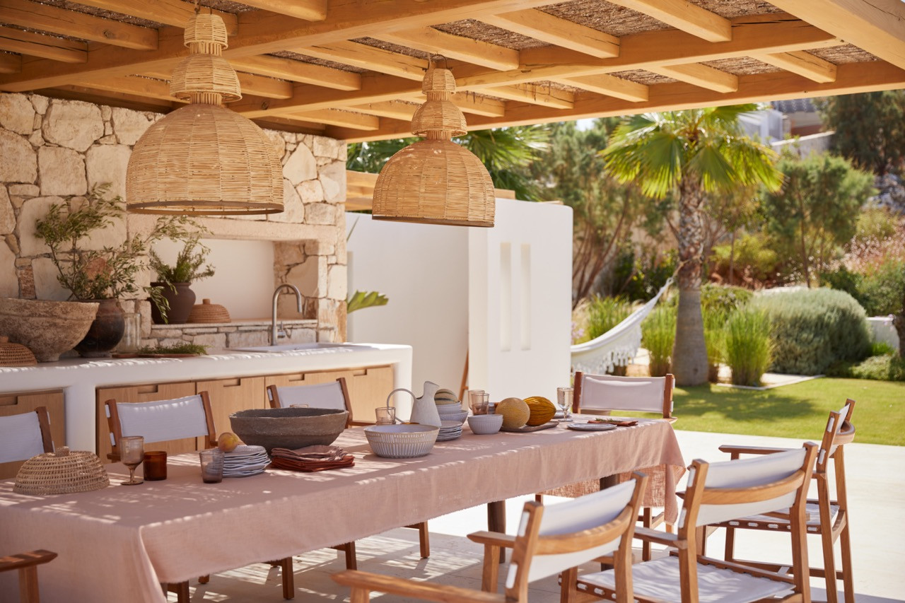 The outdoor dining area overlooks a lawn with palm trees and views across the olive grove towards the Mediterranean landscape