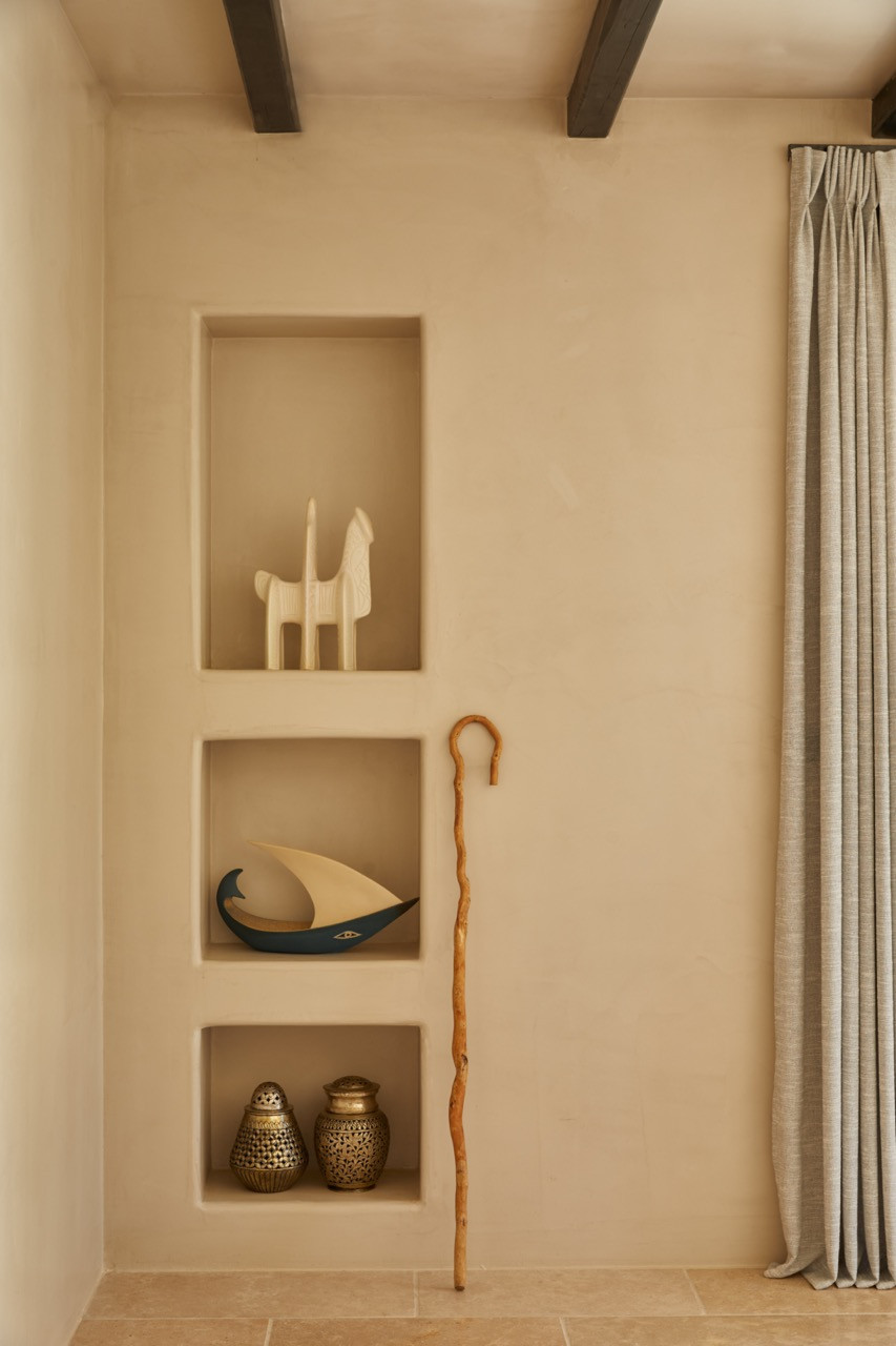 Built-in wall niches hold wooden figurines, a ceramic boat sculpture and patterned metal vessels with a carved wooden walking stick