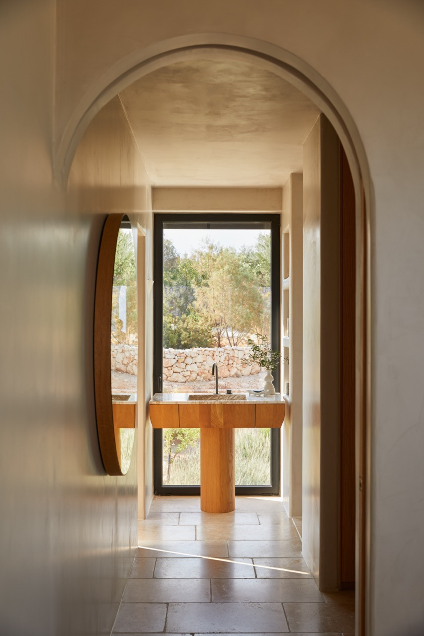 Curved archway and textured plaster walls guide the eye toward a bathroom vanity with views of the stone-walled landscape