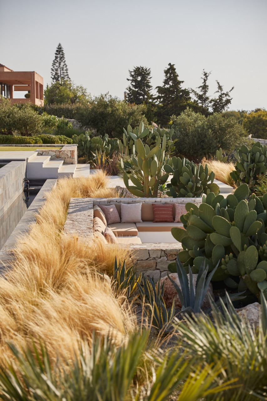 Built-in stone seating nestled among Mediterranean plantings creates an intimate gathering spot with views across the property