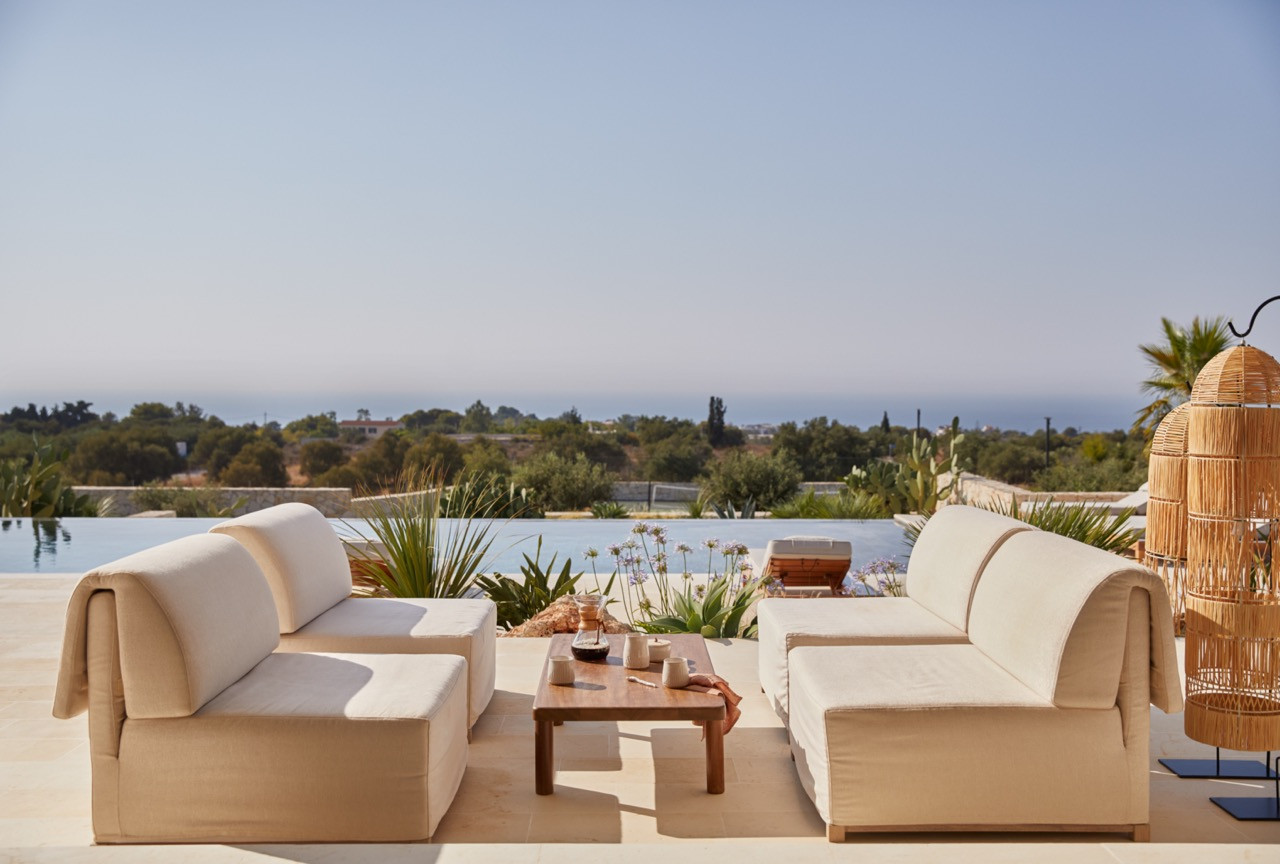 Curved outdoor furniture on the pool terrace frames views across the Mediterranean landscape toward the distant sea
