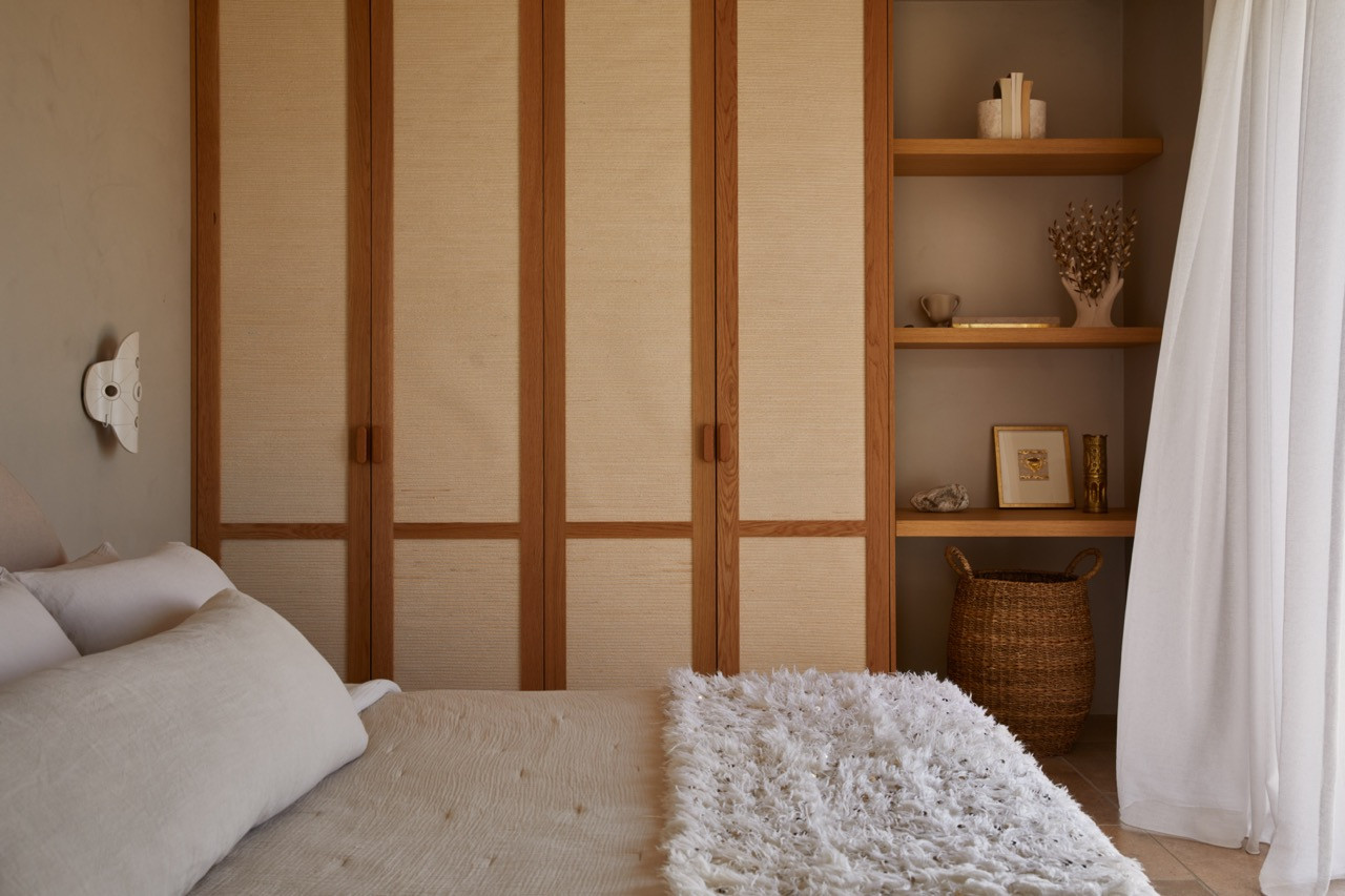 Custom wooden wardrobes with natural fiber panel inserts complement open shelving displaying carefully curated objects in the bedroom