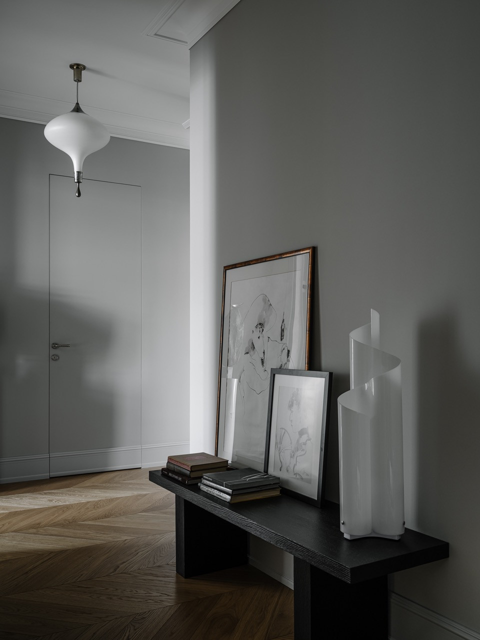 Hallway with herringbone parquet flooring, concealed door, vintage pendant light and console displaying artworks in natural wood frames