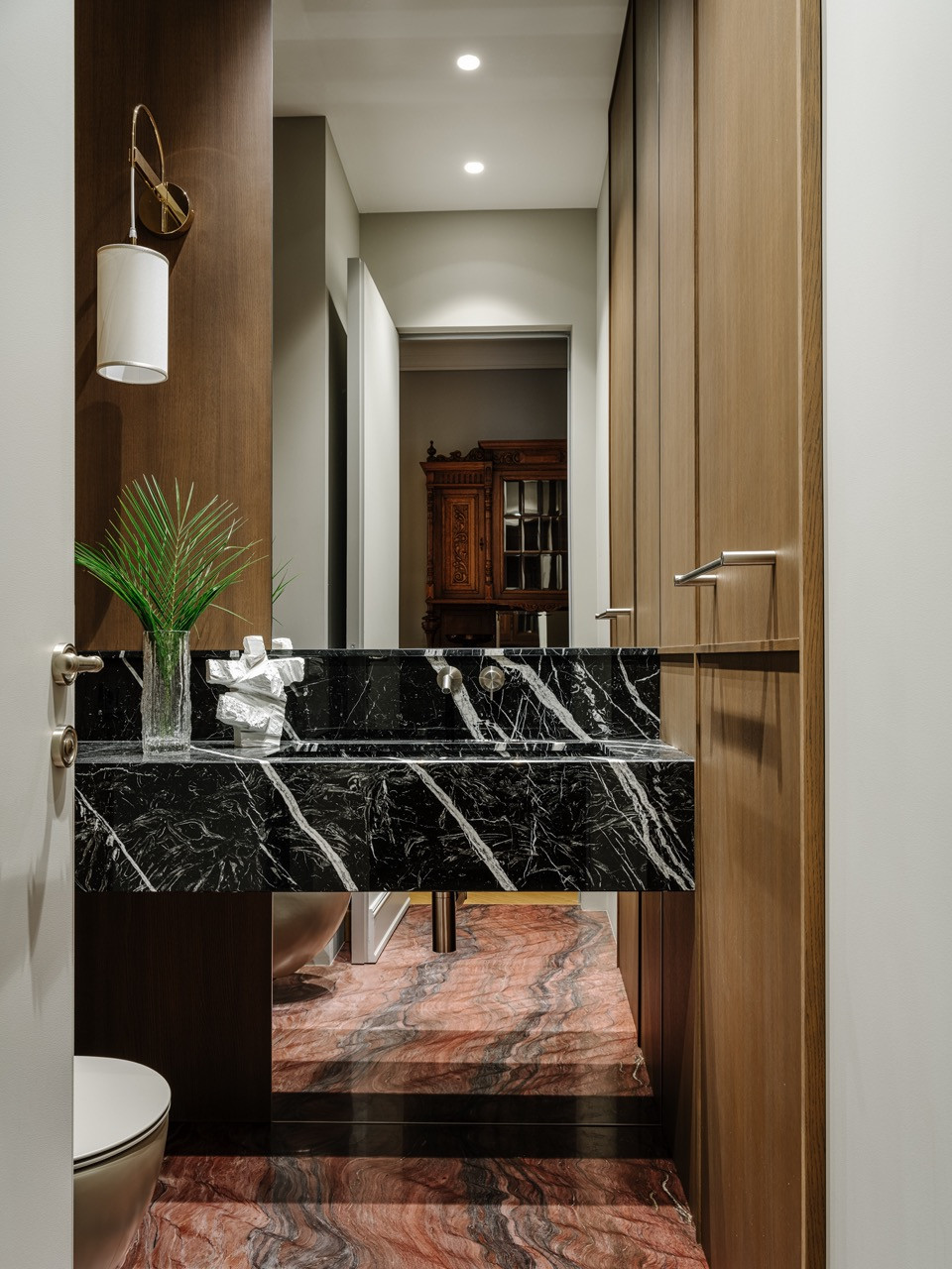 A powder room featuring dramatic black and coral marble surfaces with wood panelling