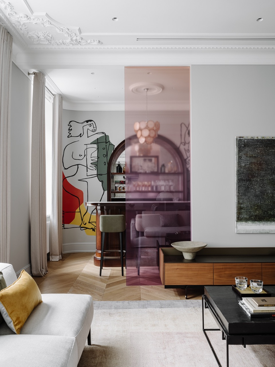 Living room with a custom pink glass partition revealing a glimpse of the bar area beyond, featuring artwork in a natural wood frame