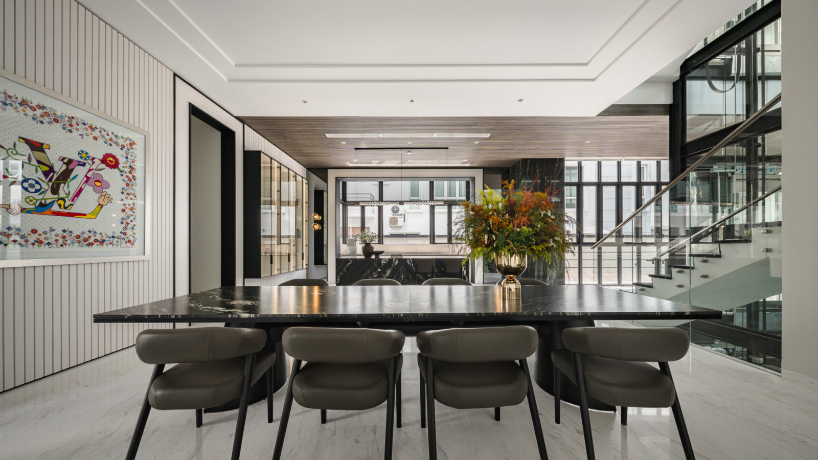 The dining area features a dramatic black marble table that serves as both functional furniture and sculptural element, with soaring ceilings that showcase the home’s remarkable natural light quality